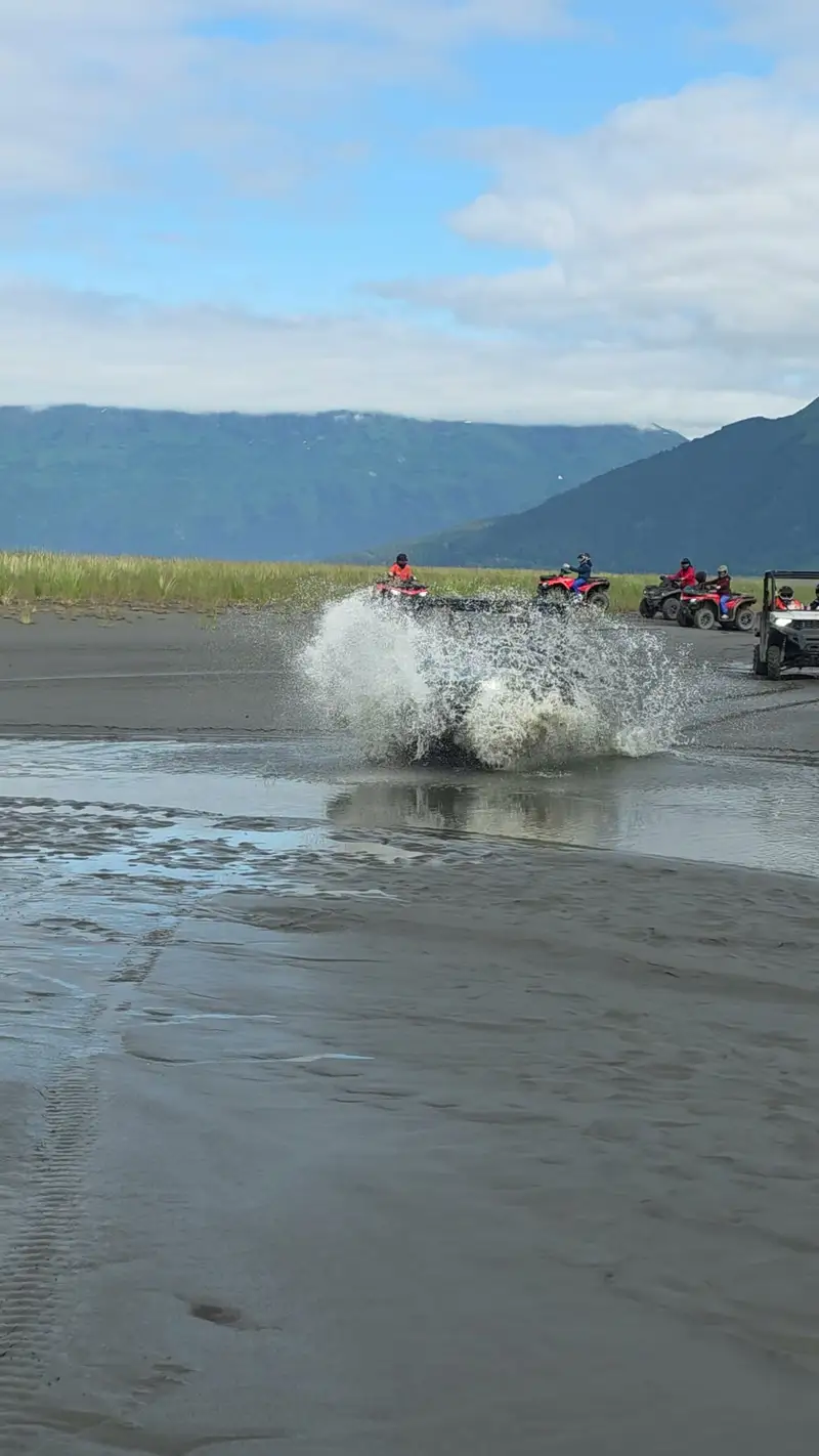 ATV throwing a wall of spray as it crosses a tidal channel, the rest of the group following behind