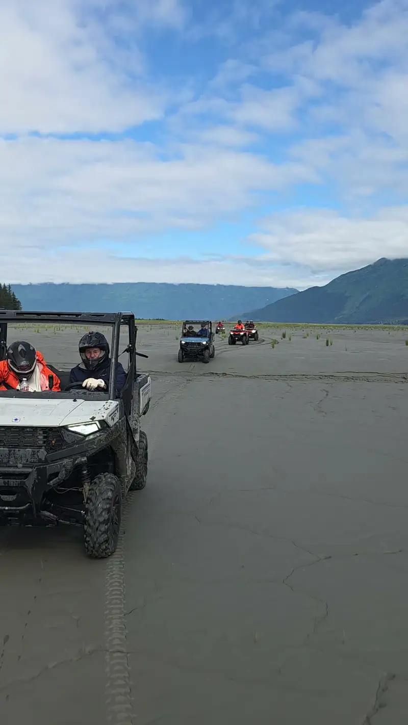 Ranger side-by-side leading a convoy of ATVs back across the flats toward the camera, mountains behind