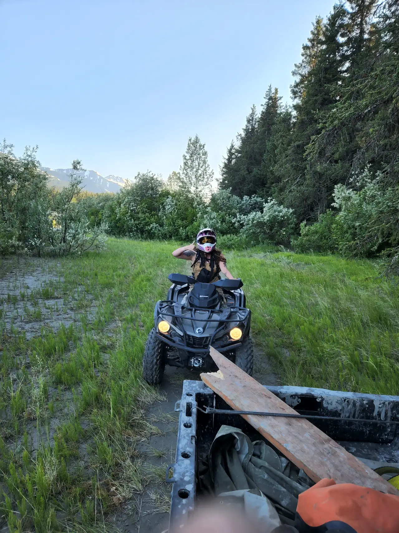 ATV and rider parked in a green meadow above Turnagain Arm, spruce and mountains behind