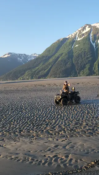 ATV and rider on the black-sand tidal flats of Turnagain Arm below snow-capped peaks