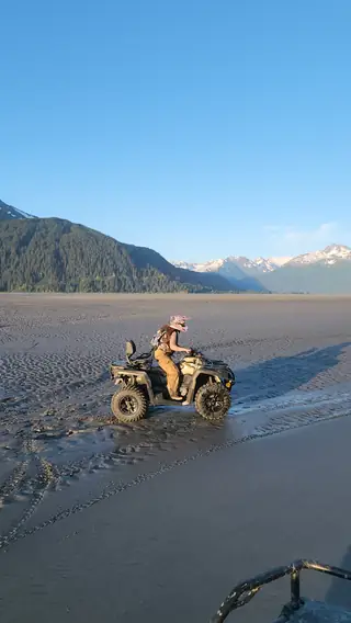 Rider crossing the Turnagain Arm tidal flats on an ATV with snowy mountains behind